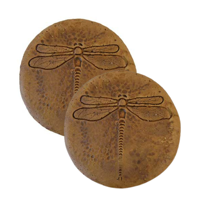Two handcrafted dragonfly garden stepping stones with a rustic autumn wheat finish, placed along a path surrounded by colorful garden plants.